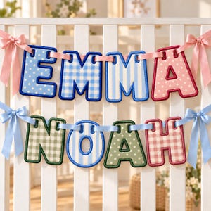 May include: A two-row fabric letter banner spelling EMMA and NOAH. The letters feature various patterns including blue and white polka dots, gingham, and stripes, and pink polka dots and gingham. The banner is held by light pink and blue ribbons.