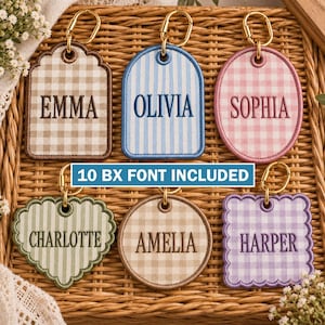 Pode incluir: Seis porta-chaves de tecido bordado com fechos de mosquetão dourados, apresentando várias formas e padrões axadrezados ou listrados. Cada porta-chaves exibe um nome personalizado: EMMA, OLIVIA, SOPHIA, CHARLOTTE, AMELIA e HARPER. O texto diz 10 BX FONT INCLUDED.