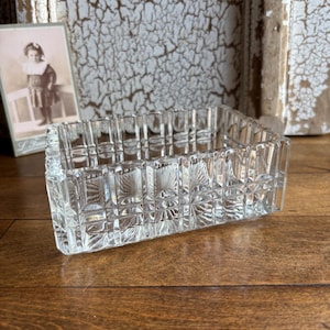 May include: A rectangular clear glass dish featuring a geometric grid pattern of raised squares and vertical lines. The glass has a thick, faceted construction with a repeating textured design across all four sides, creating a prismatic effect.