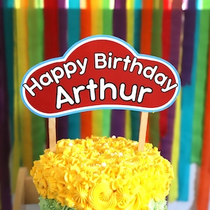 May include: A yellow frosted cake with a red and blue birthday sign that says "Happy Birthday Arthur" on top.