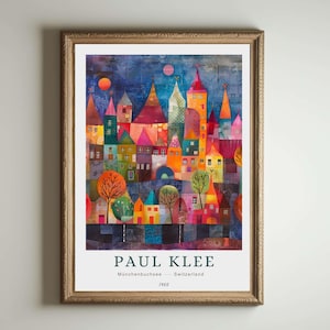 Op de afbeelding: Een ingelijste kunstdruk van een kleurrijk stadsgezicht van Paul Klee. Het kunstwerk toont levendige gebouwen met puntige daken in tinten rood, oranje, geel en blauw. De prent bevat de naam van de kunstenaar, de titel "Münchenbuchsee" en het jaar 1960.