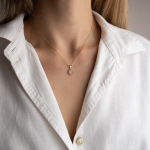 A model from a distance facing straight towards the light, highlighting the play of light on the 14K solid gold, circle shape Rose Quartz necklace, showcasing its unique reflections.