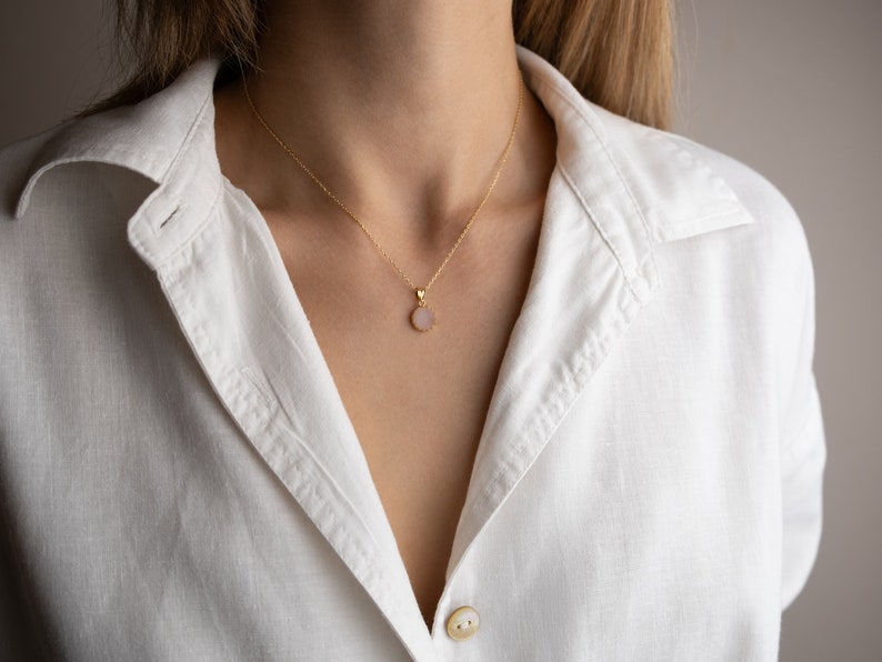 A model from a distance facing straight towards the light, highlighting the play of light on the 14K solid gold, circle shape Rose Quartz necklace, showcasing its unique reflections.