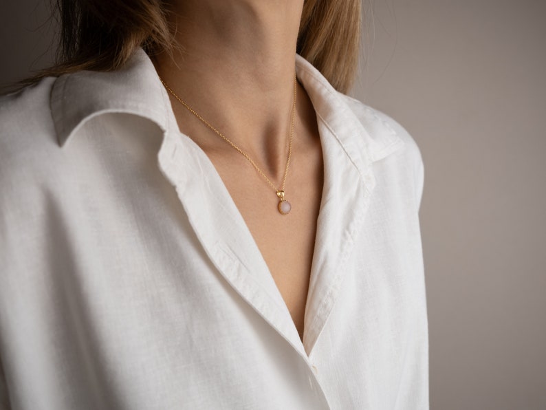 Model facing towards the light, highlighting the play of light on the 14K solid gold, circle shape Rose Quartz necklace, showcasing its unique reflections.