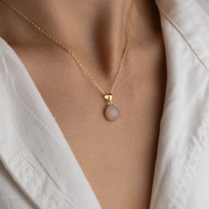 Close up of a model facing straight towards the light, highlighting the play of light on the 14K solid gold, circle shape Rose Quartz necklace, showcasing its unique reflections.