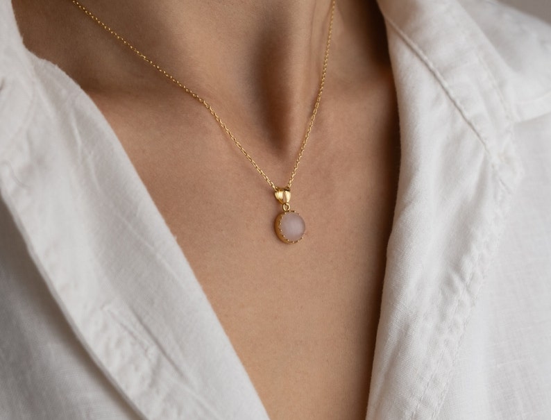 Close up of a model facing straight towards the light, highlighting the play of light on the 14K solid gold, circle shape Rose Quartz necklace, showcasing its unique reflections.