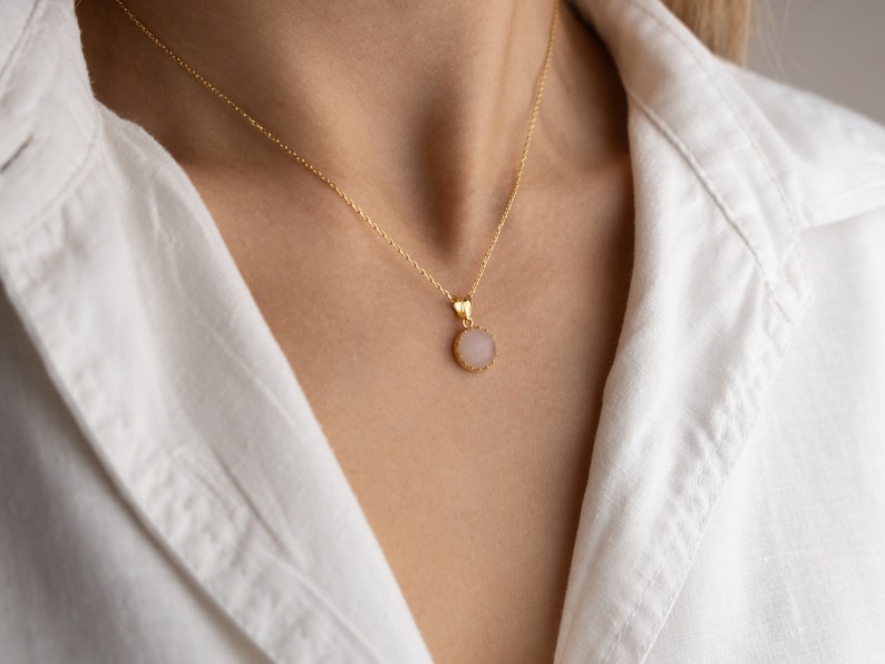 Close up of a model facing straight towards the light, highlighting the play of light on the 14K solid gold, circle shape Rose Quartz necklace, showcasing its unique reflections.