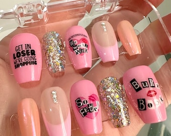 May include: Pink and nude press-on nails with various designs, including "Get in Loser, We're Going Shopping", "On Wednesdays We Wear Pink", "So Fetch", glitter, and "Burra Book".