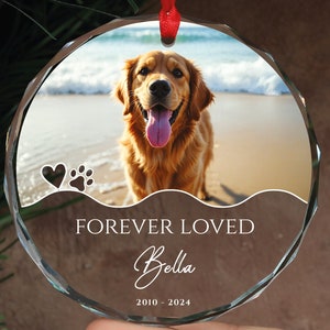 May include: A round glass ornament with a photo of a golden retriever dog on a beach. The ornament has the text "FOREVER LOVED Bella 2010 - 2024" printed on it.