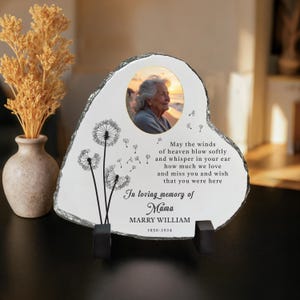 May include: Heart-shaped memorial stone with a photo of an elderly woman. The stone features a dandelion design and the text "In loving memory of Mama, Marry William, 1950-2024." Includes a poem about missing a loved one.