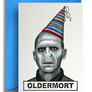 May include: Greeting card with a portrait of a pale-skinned man wearing a party hat with colorful stripes and streamers. The card has the word "OLDERMORT" in a rectangular box at the bottom. The card is inside a blue envelope.