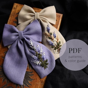 Könnte beinhalten: Zwei Stoffschleifen mit gestickten Lavendelblüten. Die Schleife links ist lila und die Schleife rechts ist beige. Der Text "PDF patterns & color guide" befindet sich auf einem weißen Kreis.