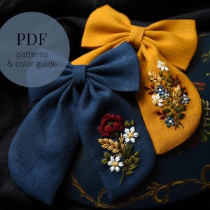 Peut inclure: Deux nœuds pour cheveux en tissu, un bleu marine et un jaune moutarde, avec des motifs floraux brodés. Le nœud bleu marine présente une fleur rouge et des marguerites blanches. Le nœud jaune a un bouquet de fleurs. Le texte à gauche dit "PDF patterns & color guide."