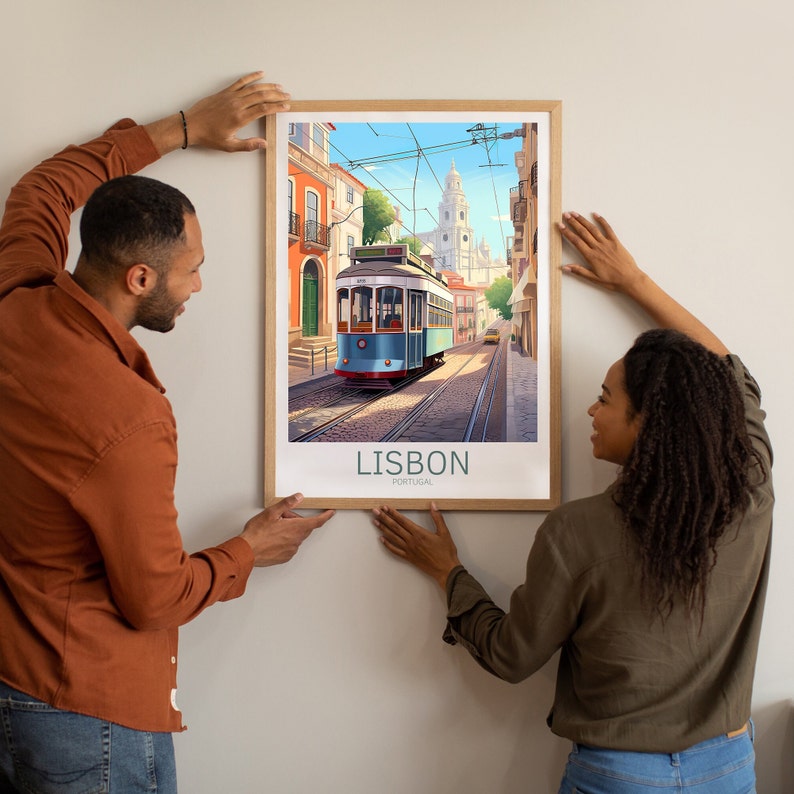 Op de afbeelding: Een vintage poster met een blauwe en witte tram die door een straat in Lissabon, Portugal, rijdt. De poster heeft een bruine lijst en de tekst "LISBON, PORTUGAL" onderaan.