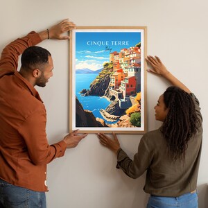 May include: A framed poster with a colorful illustration of the Cinque Terre region of Italy. The poster features a seaside town with colorful buildings, a blue ocean, and green cliffs. The text "Cinque Terre Italy" is printed at the top of the poster.