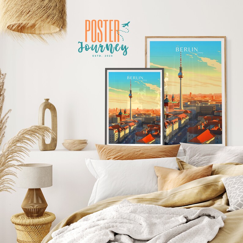 May include: Two framed travel posters with a vintage aesthetic featuring the Berlin skyline with the iconic TV Tower. The posters are in different sizes and are hanging on a white wall above a bed with a white blanket and brown pillows.