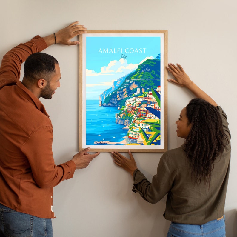 May include: A framed illustration of the Amalfi Coast in Italy. The illustration features a colorful depiction of the coastline with buildings, cliffs, and the sea. The text "Amalfi Coast Italy" is printed at the top of the illustration.