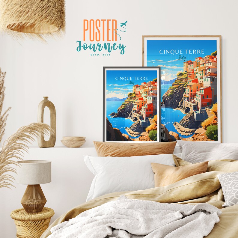 May include: Two framed travel posters with a colorful illustration of the Cinque Terre region in Italy. The posters are hanging on a white wall above a bed with white and brown bedding.