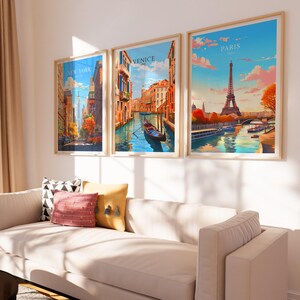 Puede incluir: Tres carteles de viaje enmarcados con paisajes urbanos. Los carteles est&aacute;n colgados en una pared blanca sobre un sof&aacute; blanco con almohadas. Los carteles muestran im&aacute;genes de la ciudad de Nueva York, Venecia y Par&iacute;s.