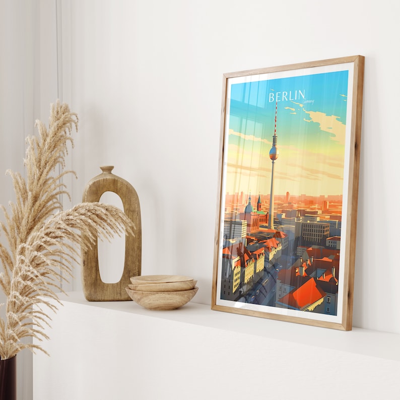 May include: A framed print of a cityscape with the Berlin Television Tower in the center. The print has a vintage travel poster aesthetic with a blue sky and orange and red buildings.