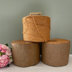 Può includere: Tre bobine di spago marrone naturale, ciascuna avvolta in carta marrone. La bobina superiore ha un'etichetta che recita "Bout a tirer".