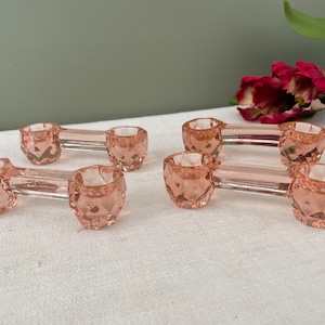 May include: Set of six pink glass salt cellars, each with a rounded, faceted design. The cellars are connected in pairs by a clear glass stem.