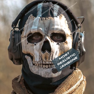 Peut inclure: Gros plan d'une personne portant un masque de crâne avec un passe-montagne noir et un casque. Le masque est blanc cassé avec des détails noirs et une mâchoire réaliste. Le texte "MOST REALISTIC JAWBONE" est sur une étiquette.