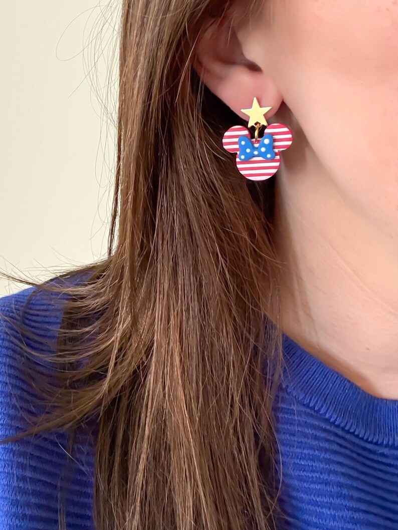 Puede incluir: Pendientes con forma de Minnie Mouse a rayas rojas y blancas, con un lazo azul y una estrella dorada. Un accesorio festivo, perfecto para a&ntilde;adir un toque de diversi&oacute;n a cualquier atuendo.