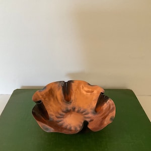 May include: A copper bowl with a scalloped edge. The bowl is sitting on a green book.