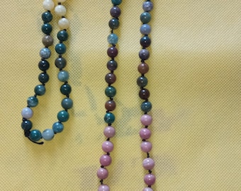 May include: A multi-colored gemstone mala necklace with a black tassel. The necklace features beads in shades of green, brown, white, and pink.