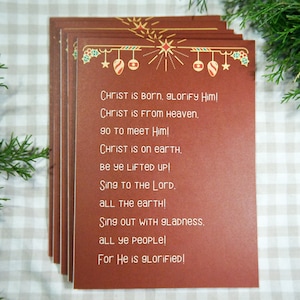 Könnte beinhalten: Ein Stapel roter Karten mit weißem Rand und goldenen Akzenten. Die Karten zeigen ein Weihnachtsmotiv mit Ornamenten und einem Stern. Der Text auf den Karten lautet: "CHRIST is Born, glorify Him! CHRIST is From Heaven. 90 to meet Him! Christ is on earth, Be Ye LIFTED UP! Sing TO THE LOND. ALL THE earTHI Sing OUT WITH 9Ladness. ALL YE PEOPLE! For He is glorified!"