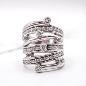 May include: A silver ring with a multi-layered design. The ring features multiple bands, some adorned with small, clear gemstones. The ring has a modern, abstract style, with a polished finish. The ring is set against a white background.