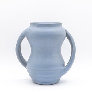 May include: A light blue ceramic vessel featuring a wide, rounded body with a narrow neck and two symmetrical, curved handles extending from the upper sides to the lower midsection, finished with a matte texture and subtle horizontal ridges.