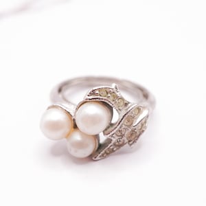 May include: A silver ring with three white pearls and a leaf design with clear rhinestones.