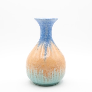 May include: A ceramic vase with a blue neck, transitioning to a tan midsection, and ending with a turquoise base. The vase has a rounded body and a narrow neck, suitable for displaying flowers or as a decorative piece.