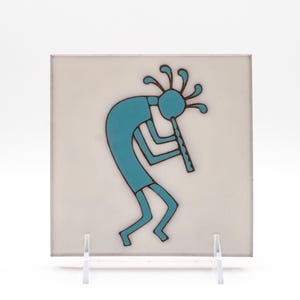 May include: A square ceramic tile featuring a turquoise-colored Kokopelli figure playing a flute. The figure is depicted in a stylized, bent-over posture with a feathered headdress, outlined in dark brown against a smooth, off-white background.