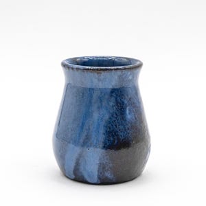 May include: A small, handcrafted ceramic vase with a rounded body and a slightly flared rim. The vase features a gradient of blue hues, transitioning from a dark, almost black base to lighter shades of blue near the top. The interior is dark blue.