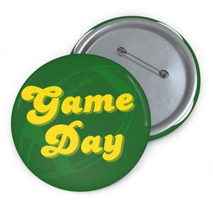 May include: Green button with a yellow "Game Day" text in a retro font. The button has a green and white football pattern in the background.