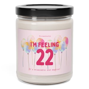 May include: A pink and white candle jar with a label that says "I'm Feeling 22 It's miserable and magical." The label has a design of colorful balloons.