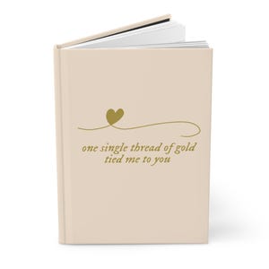 May include: A beige journal with a gold heart and the text "one single thread of gold tied me to you".