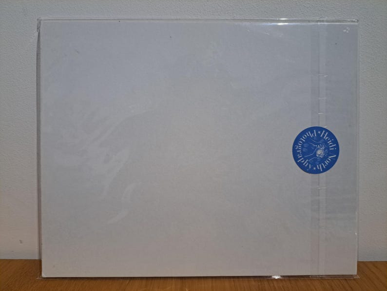 Op de afbeelding: Een blanco witte kaart met een blauwe ronde stempel waarop "Heidi South Photography" in wit staat.