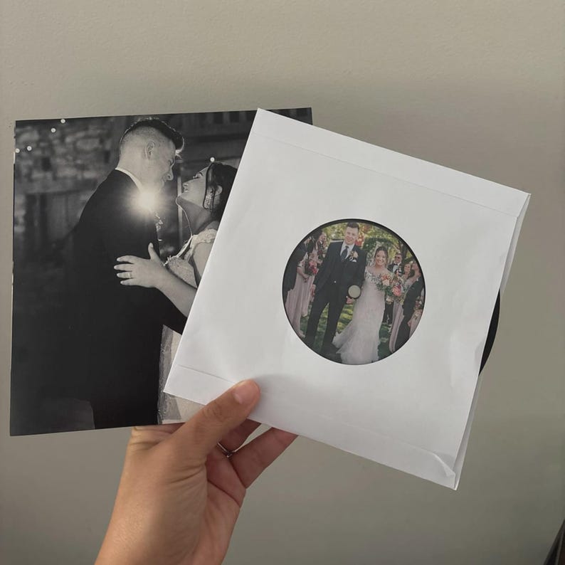May include: A black and white photograph of a couple dancing, next to a white paper sleeve with a circular color photograph of a wedding party. The sleeve holds a black disc. The images are held by a hand.