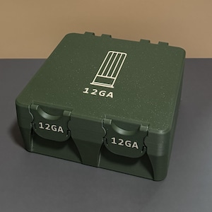 Könnte beinhalten: Ein dunkelgrüner, rechteckiger Behälter mit Klappdeckel. Der Behälter trägt den weißen Schriftzug "12GA" auf der Vorder- und Oberseite sowie eine weiße Grafik. Er ist für die Aufnahme von Munition konzipiert.