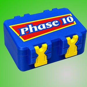 May include: A rectangular blue plastic storage case with two yellow latches on the front. The lid features a red triangular graphic with a yellow border and the white text Phase 10 printed in a bold, sans-serif font across the center of the lid.