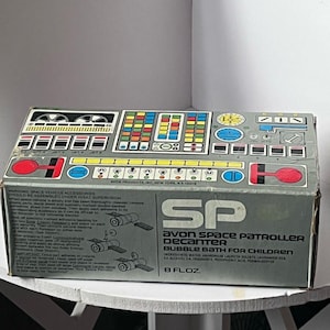 以下が含まれることがあります： Avon Space Patrollerバブルバスデカンター用の長方形のグレーの箱。上部にはボタンやダイヤルが描かれたカラフルなコントロールパネルのグラフィックがあります。側面にはSP Avon Space Patroller Bubble Bath For Children 8 Flozというテキストが表示されています。