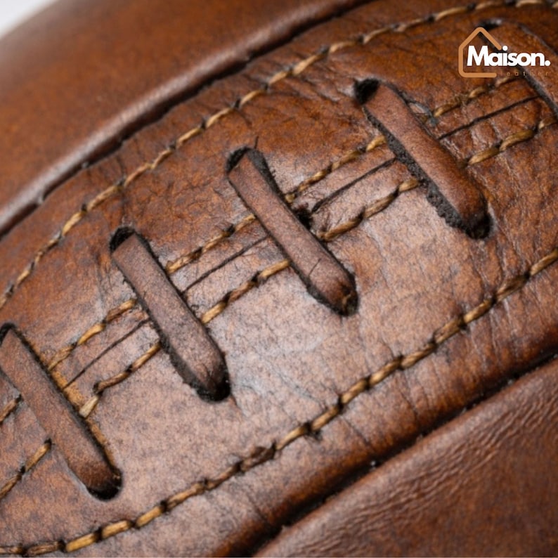 May include: Close-up of a brown leather football with stitching. The stitching is a lighter brown color and is visible throughout the image.