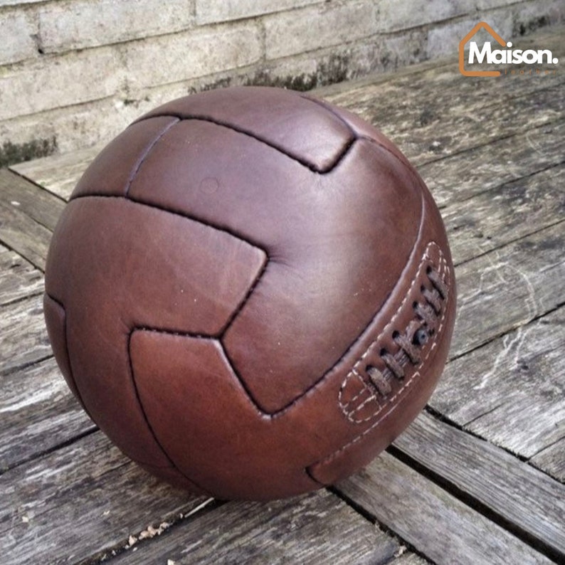 May include: A brown leather soccer ball with white stitching. The ball is on a wooden surface.