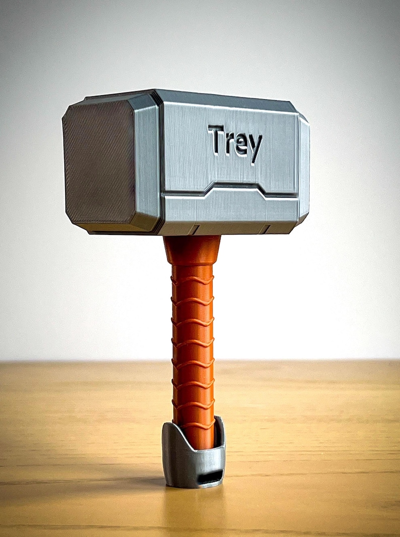 This 3D printed Thor hammer baby rattle features personalized engraving and colorful handle options like black, pink, light blue, brown, and yellow. A perfect custom baby gift and personalized baby rattle for Marvel fans.