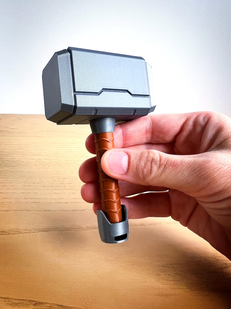 May include: A small, silver-colored hammer with a brown wooden handle. The hammer is a replica of Thor's hammer, Mjolnir, from the Marvel comics and movies.