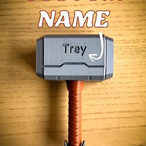 Custom engraved Thor hammer baby rattle with vibrant handle colors including pink, yellow, black, brown, and light blue. A personalized baby rattle and creative custom baby gift that’s also a fun 3D printed toy.